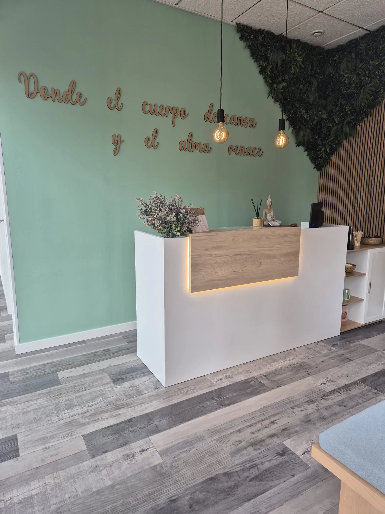 Recepción de Althaea: pared verde salvia, mostrador blanco con frente de madera y luz cálida